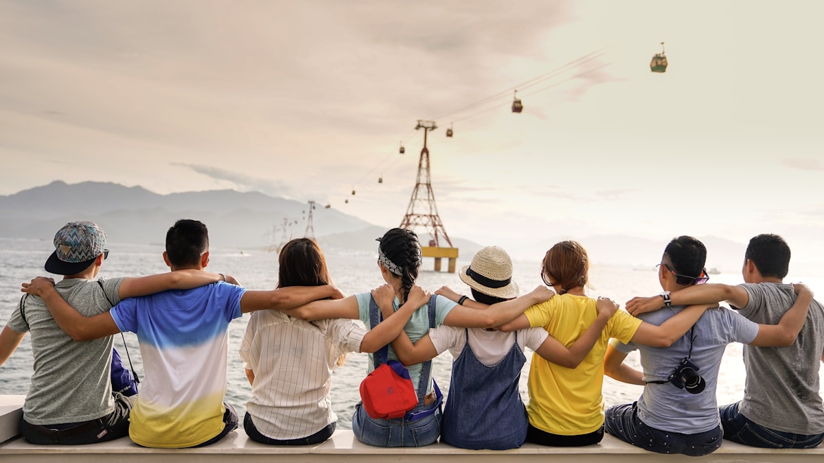 Friends sitting together with arms around each other, looking out over the water