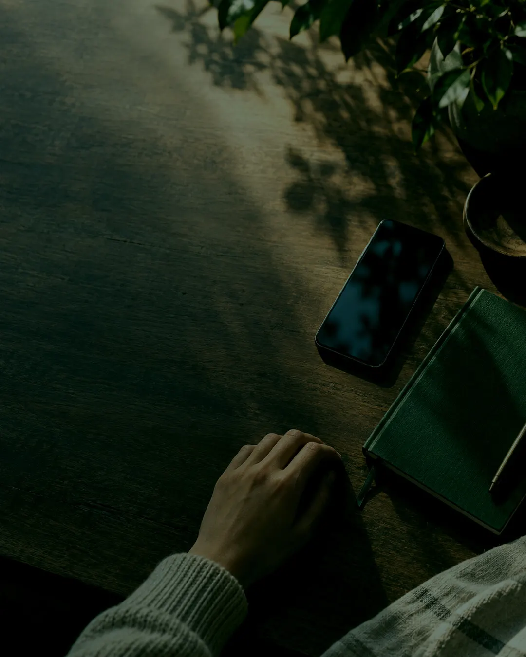 A phone and a notebook on a wooden table in dappled light
